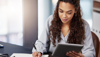 woman writing and looking at tablet